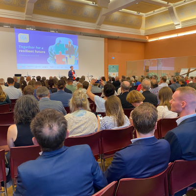 Plenary room full of people, with the moderator in front of a large screen.