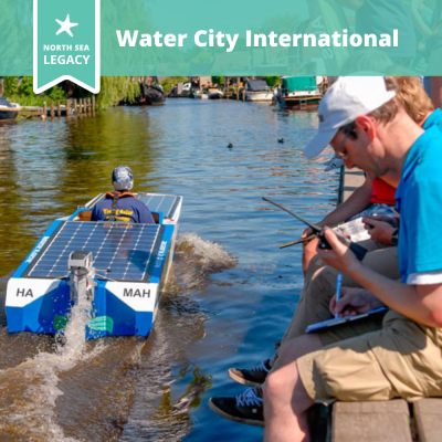 A solar boat racing along a river, with people sitting on the bank watching.