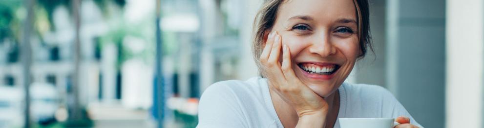 Smiling lady seated outdoors and holding a coffee cup.