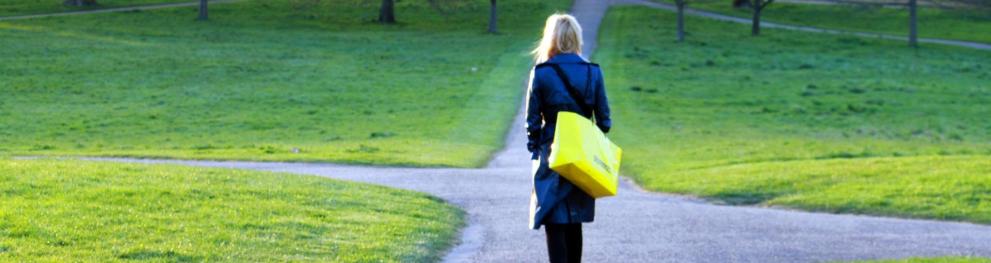 Woman carrying a large yellow bag over her shoulder walking towards a crossroads.