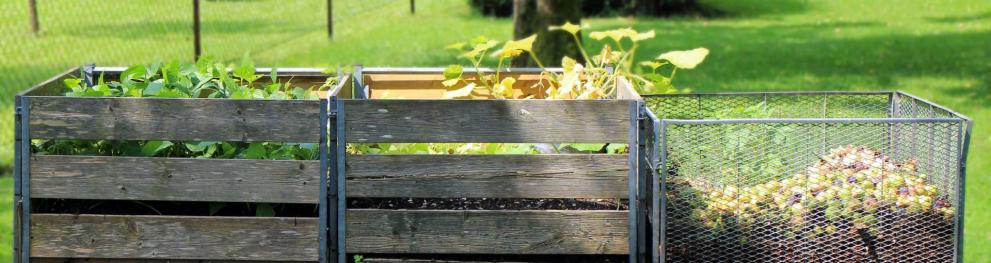 Wooden and metal crates for plant material composting, with a green field in the background. 