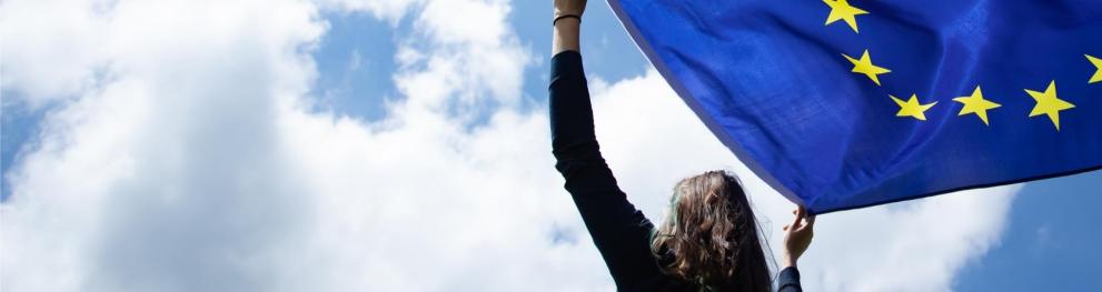 Woman holding an EU flag up against a cloudy sky.