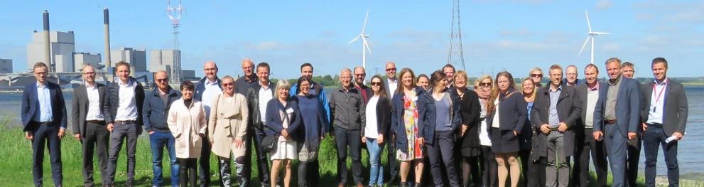 A large group of people on a lawn, with wind turbines in the background.