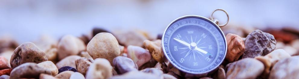 A blue compass lying on pebbles near water.