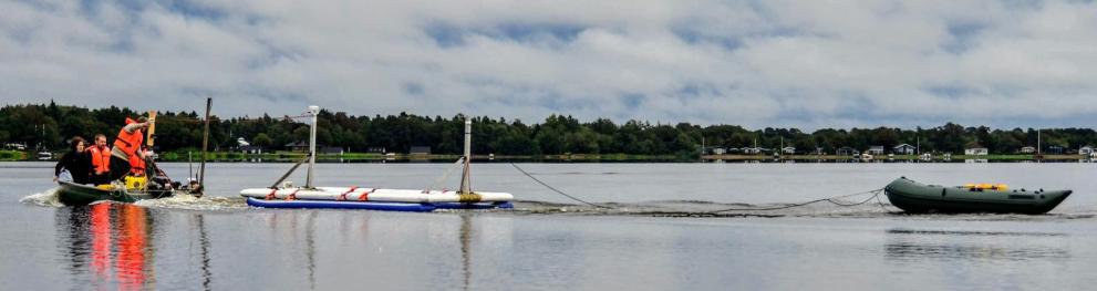 A boat with a floating device in tow, followed by a small boat with researchers.