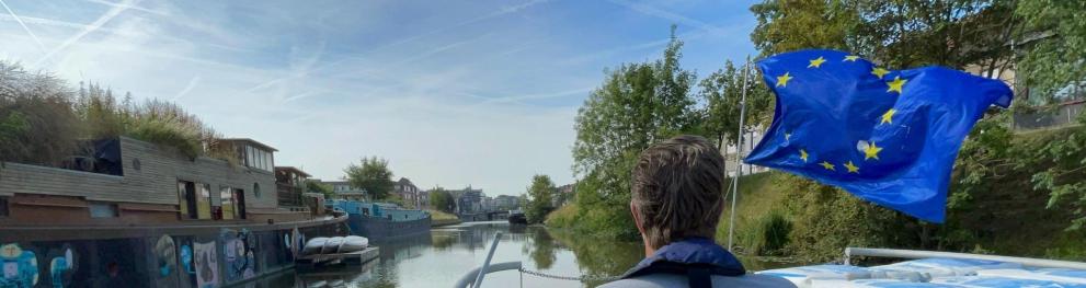 Large EU flag waving in front of a barge, with a green landscape in the background