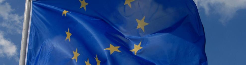 A close up of a blue EU flag with yellow stars against a blue sky