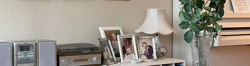 A shelf with a sound system, family photos, a lamp and some flowers next to a white piano.