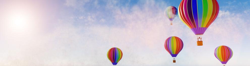 Colourful hot air baloons high up in a blue sky with white clouds