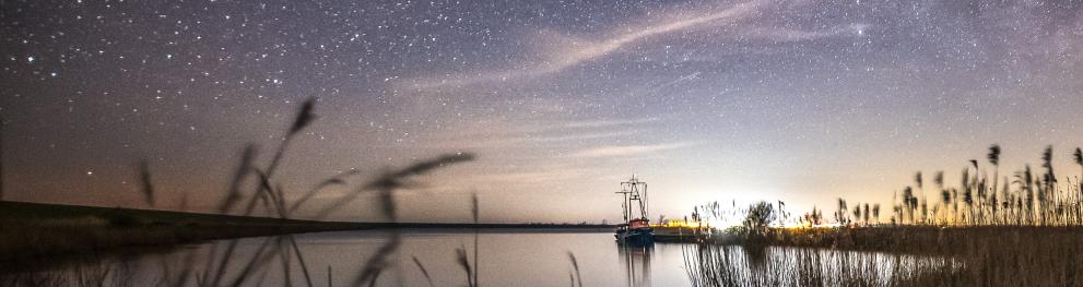 North Sea coast with a port and articfical light in the distance beneath a night sky