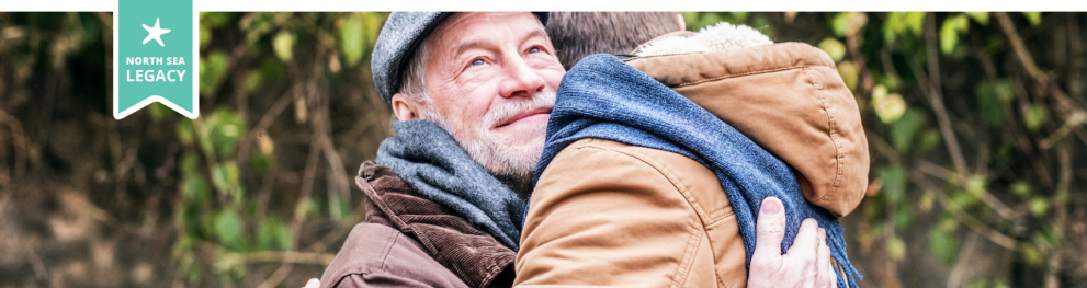 A young and an elderly man wearing winter clothes outdoors hugging one another.