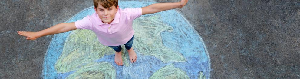Little school boy with earth globe painting with colorful chalks on ground