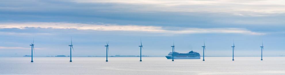A line of wind turbines and a ship in the North Sea on a calm overcast day.
