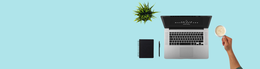 A laptop, a hand holding a cup of coffee ,a plant and notebook as seen from above.