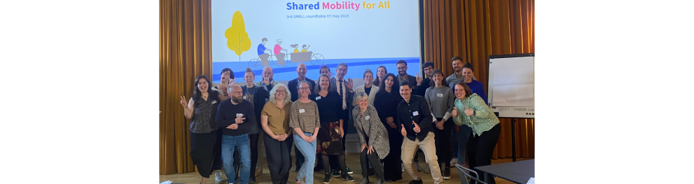 The SMALL partners and controbutors pose for a picture in front of a projector that shows the SMALL logo