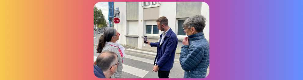 Four people are standing next to a pedrestrian crossing. One of them, a man, is showing the screen of his phone while he uses the app