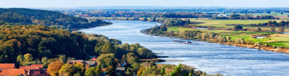 The blue Elbe River flowing through a green landscape on a clear day.