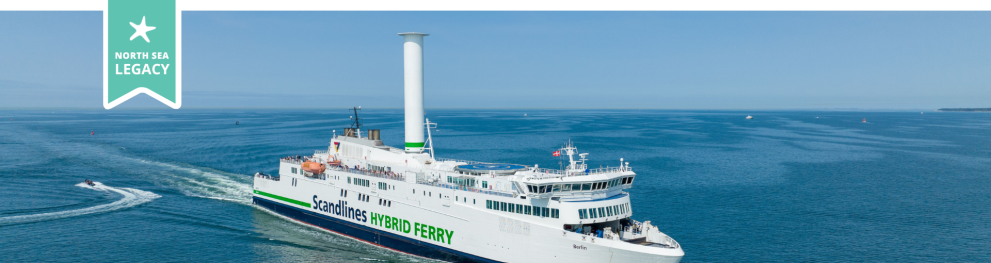 A ship retrofitted with a large cylindrical modern sail cruising through the sea in clement weather.